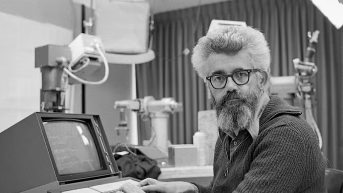 Foto em preto e branco de John McCarthy em frente a um terminal de computador antigo.